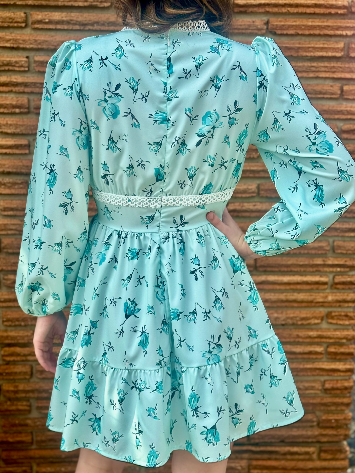 Light blue floral dress worn by a person against a brick wall.