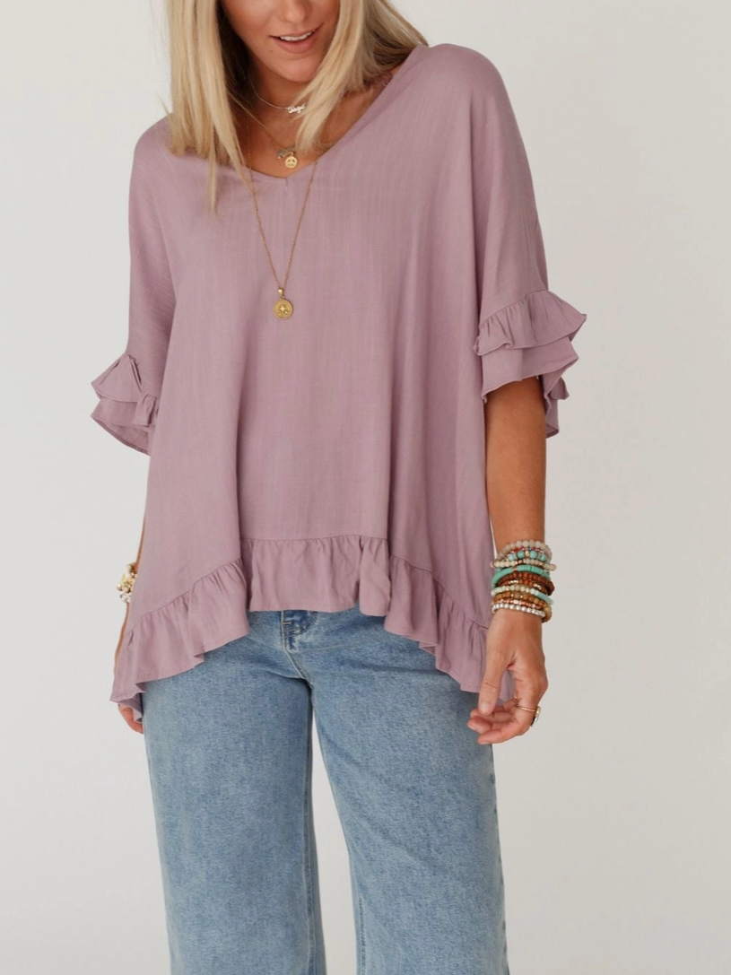 Woman wearing a mauve blouse with ruffled sleeves and blue jeans on a plain background