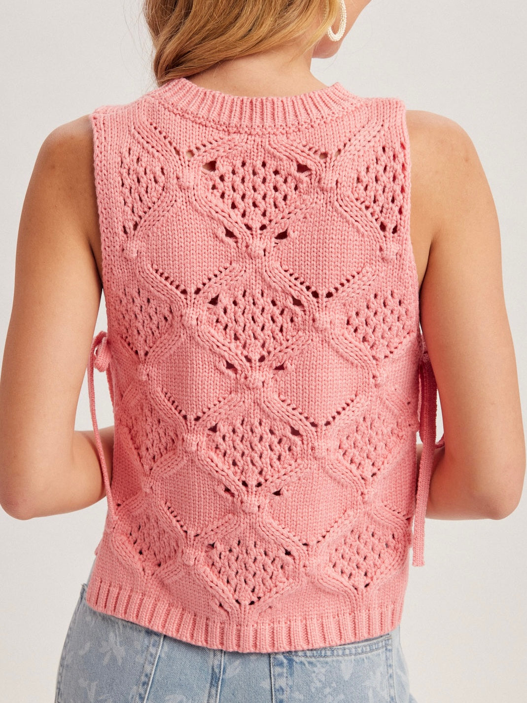 Pink knitted vest with geometric pattern worn by a person on a plain background