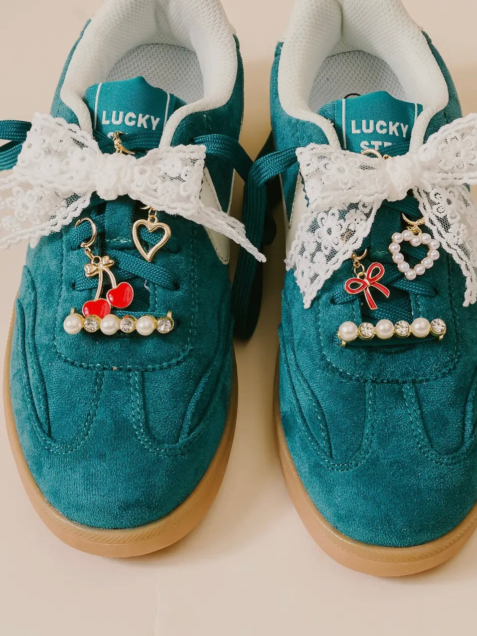 Teal sneakers with white lace and decorative charms on a light background