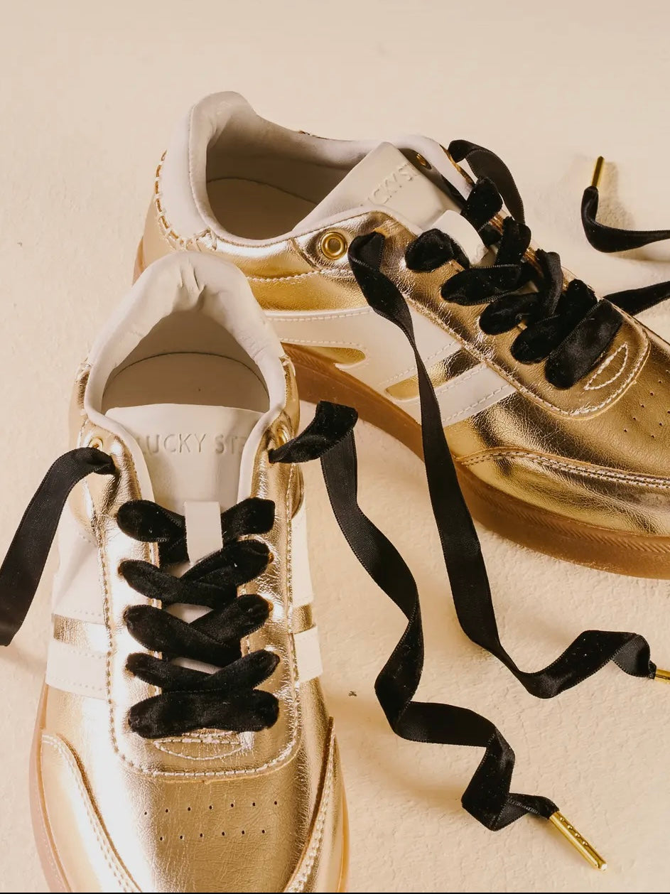 Gold sneakers with black laces on a beige background