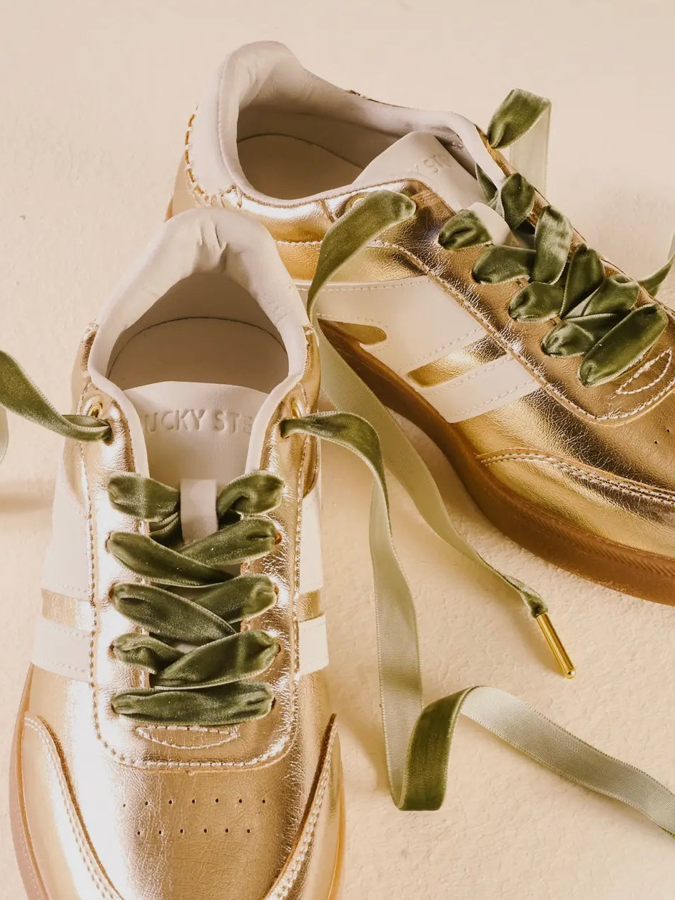 Gold sneakers with green laces on a beige background