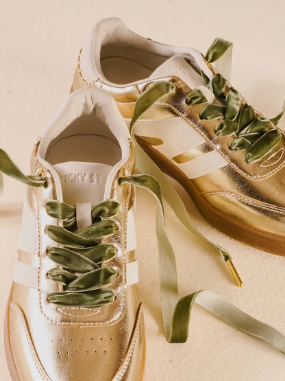 Gold sneakers with green laces on a beige background