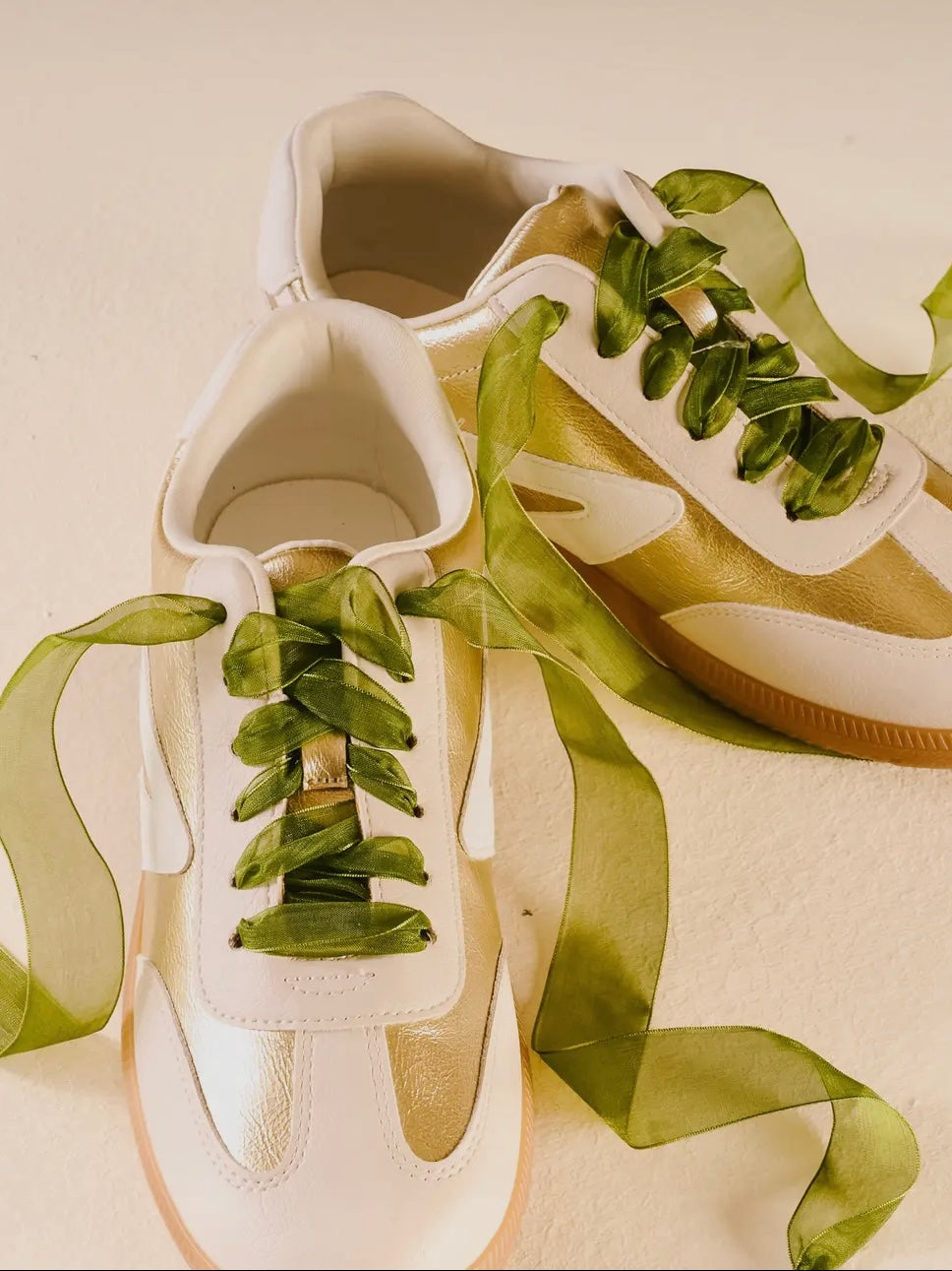 White sneakers with green ribbons on a beige background