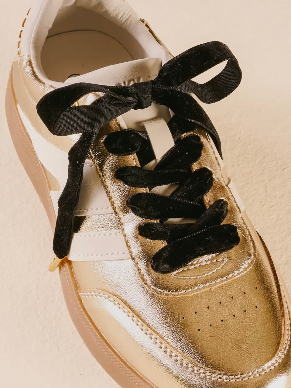 Beige sneaker with black laces on a beige background