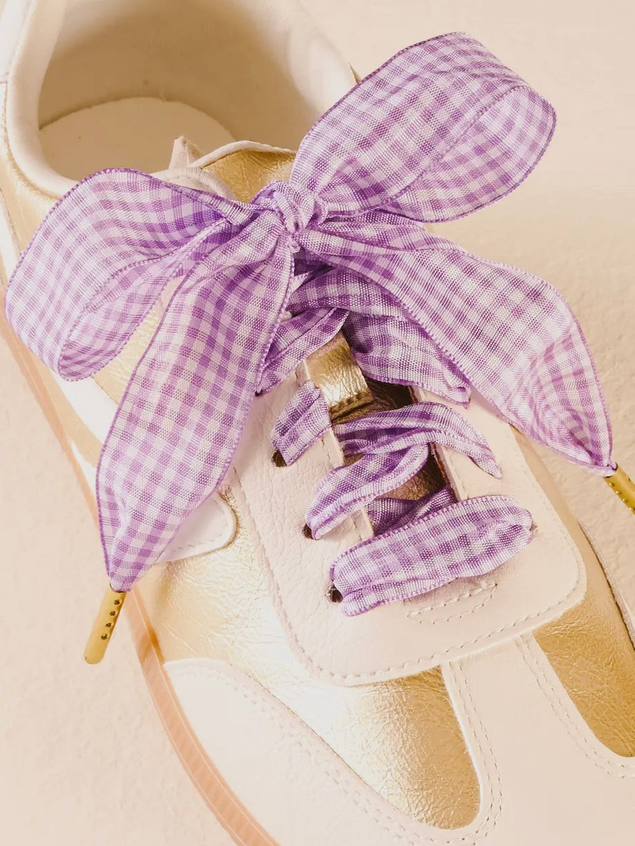 Beige baby shoe with purple gingham ribbon on a beige background