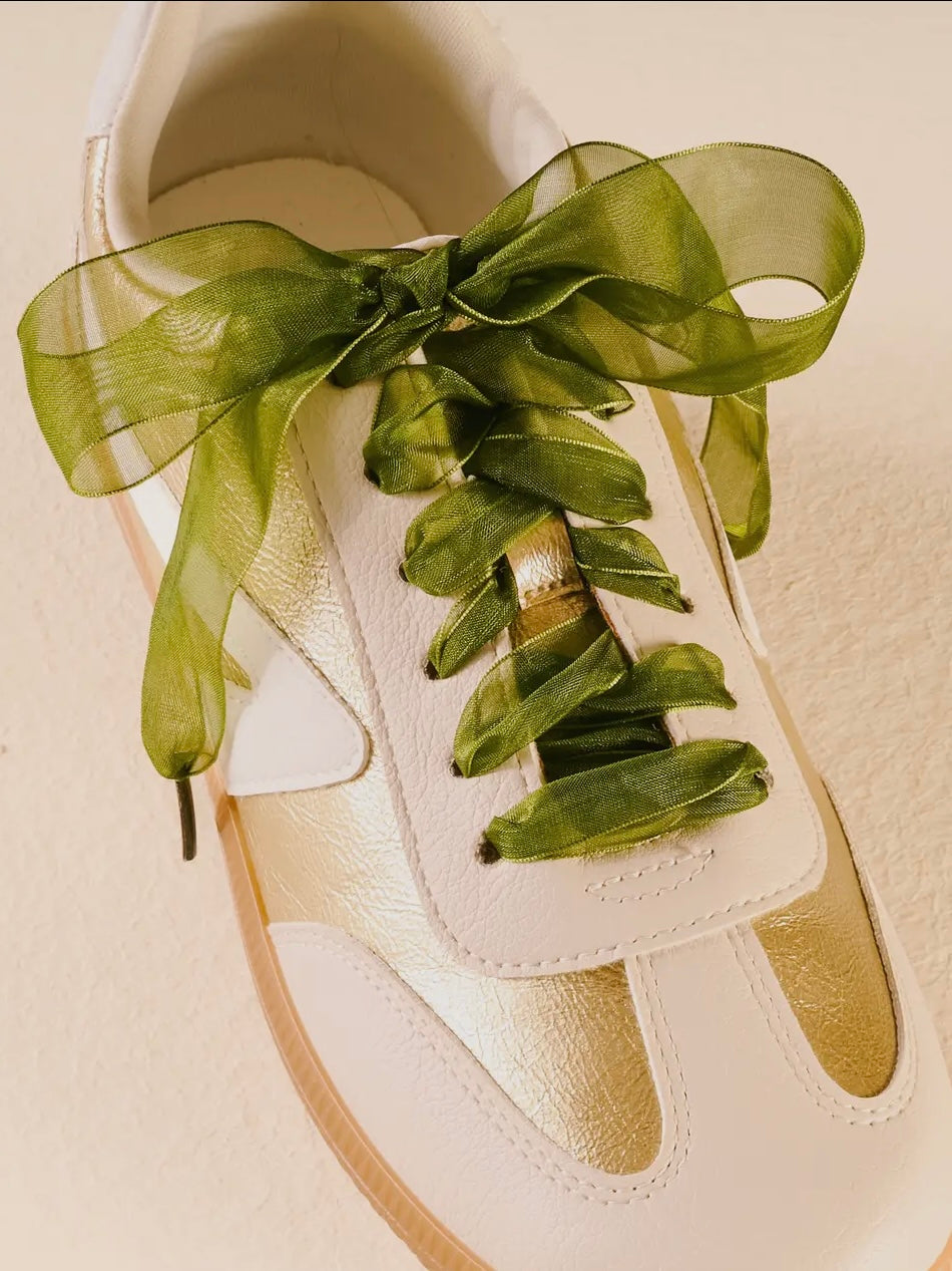 White shoe with green ribbon and leaves on a beige background
