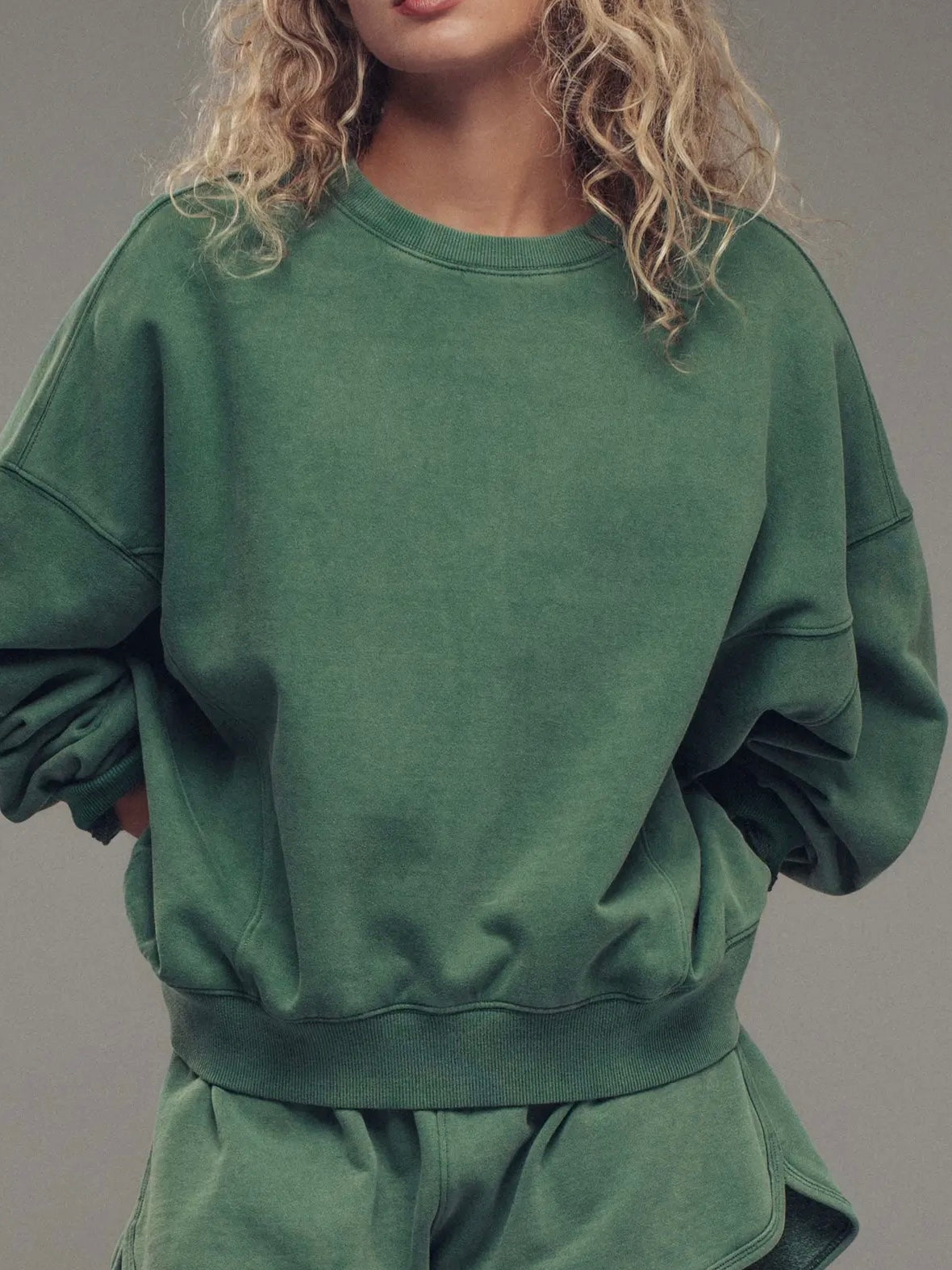 Person wearing a green sweatshirt and shorts set against a gray background
