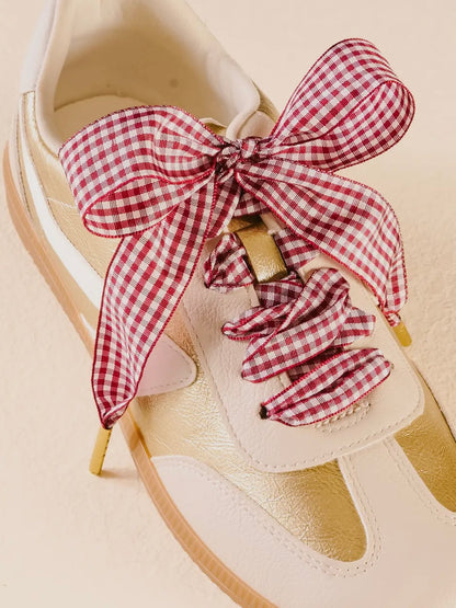 White sneaker with red and white checkered bow and scrunchie on a beige background