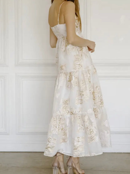Woman wearing a white floral dress against a white paneled wall.