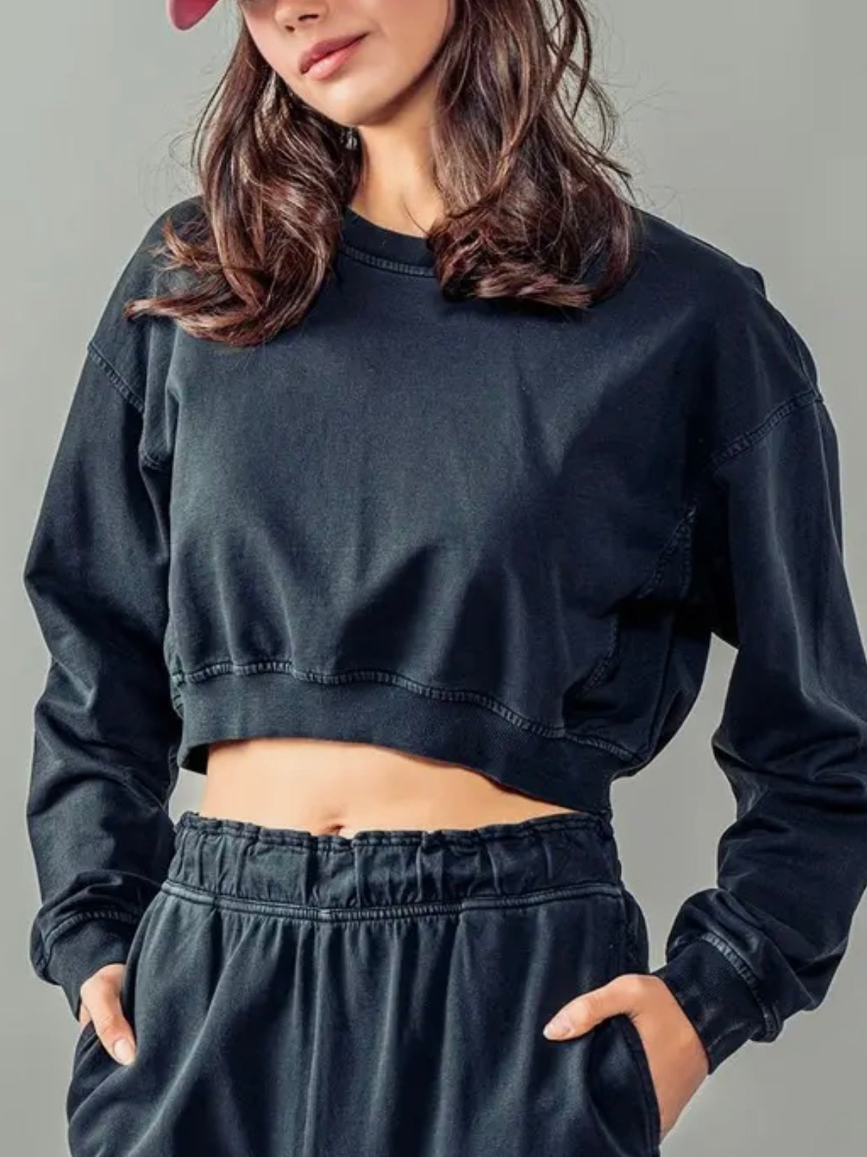 Person wearing a black cropped sweatshirt and pants on a gray background