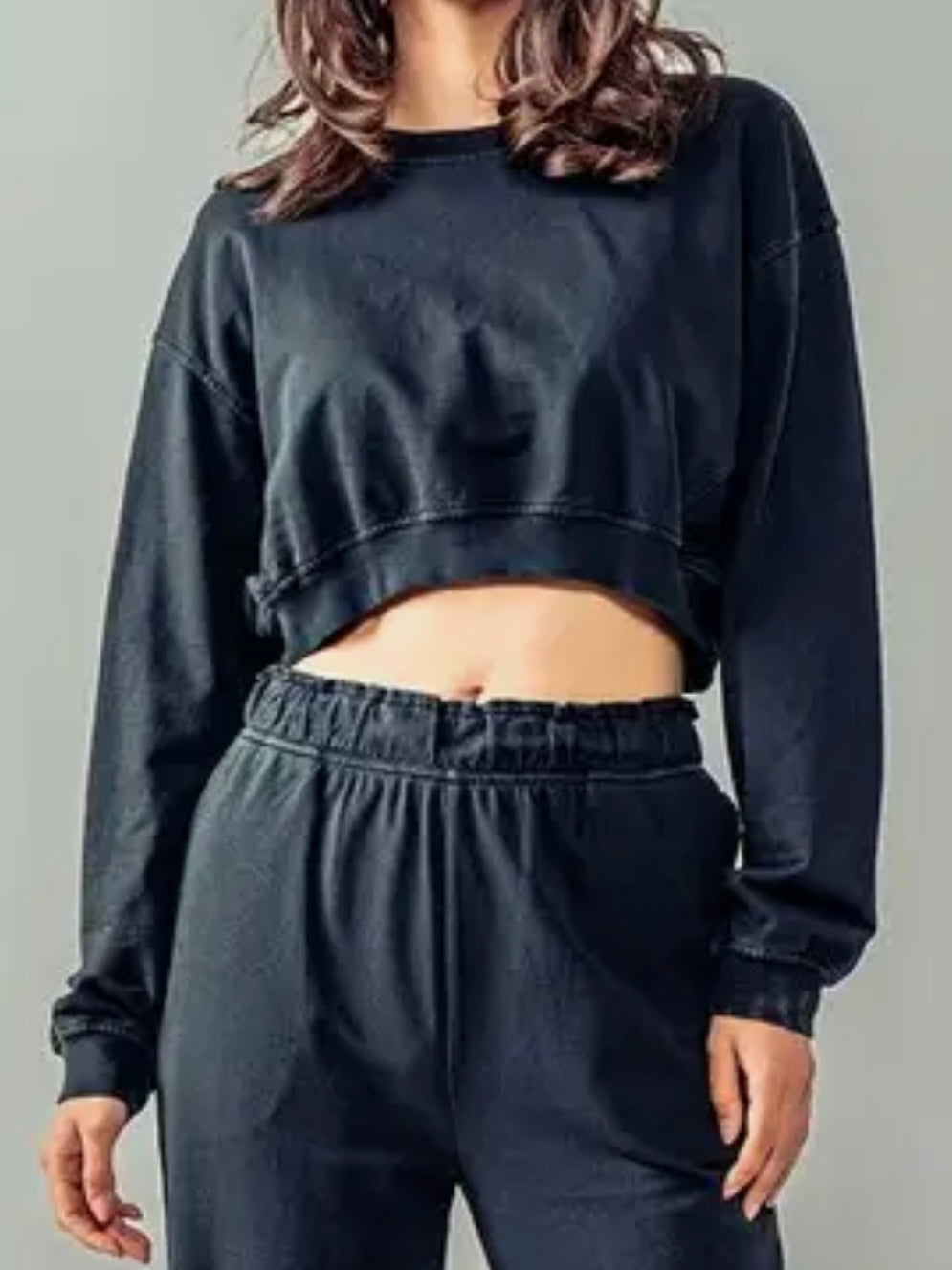 Person wearing a black cropped sweatshirt and pants on a gray background