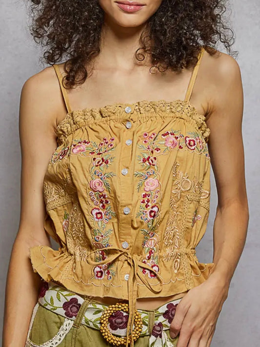 Woman wearing a mustard yellow top with floral embroidery on a plain background