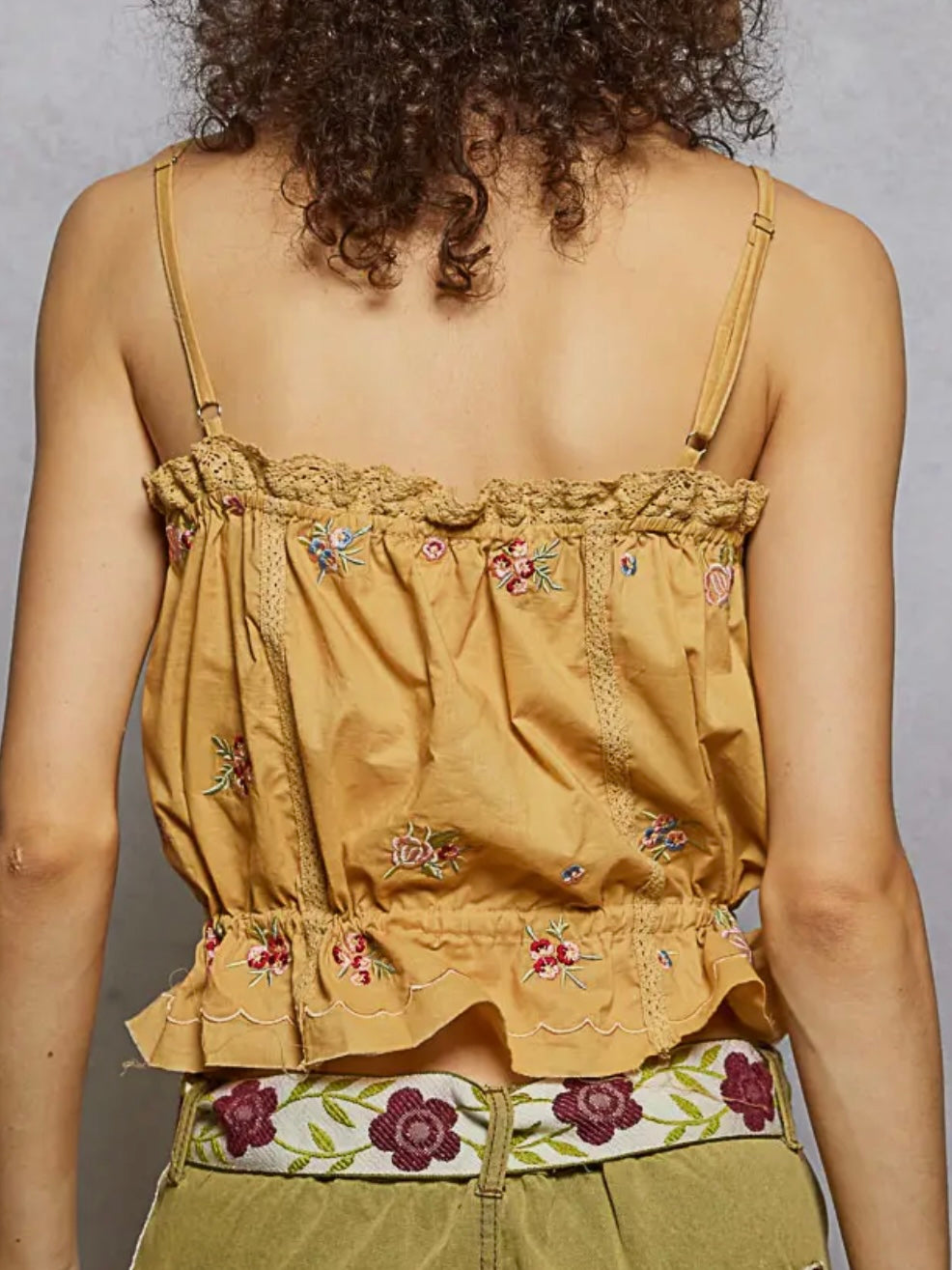 Person wearing a mustard yellow top with floral embroidery on a plain background