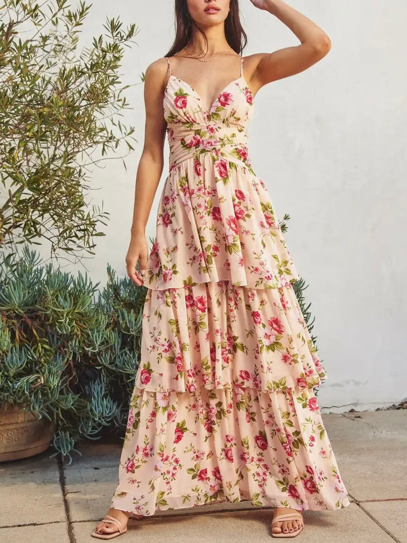 Woman wearing a floral dress standing outdoors with plants and a white wall in the background