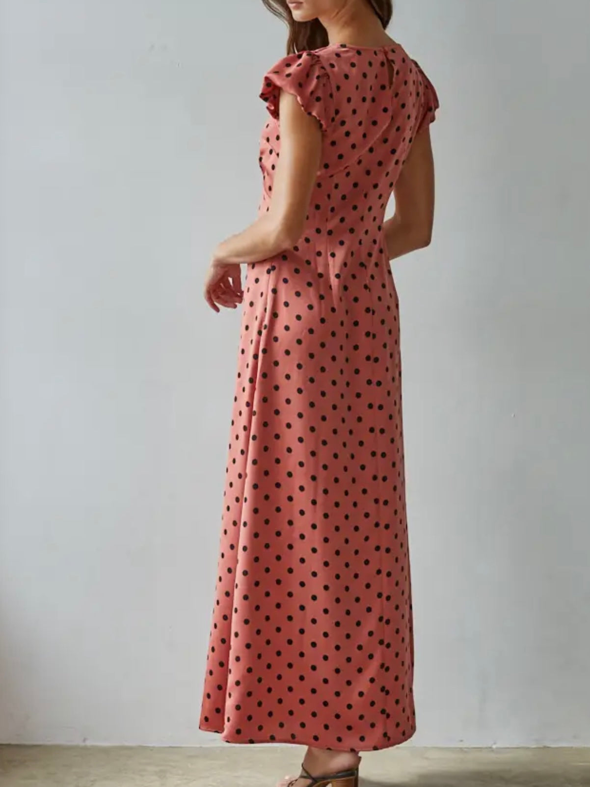 Woman wearing a pink dress with black polka dots against a plain background