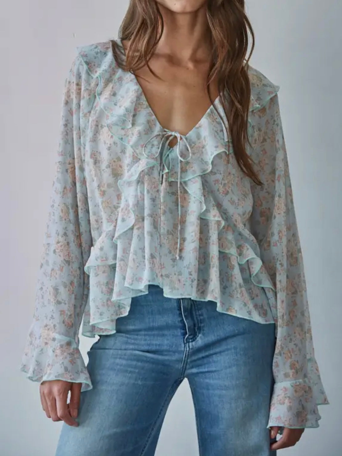 Woman wearing a floral blouse with ruffles and blue jeans on a plain background