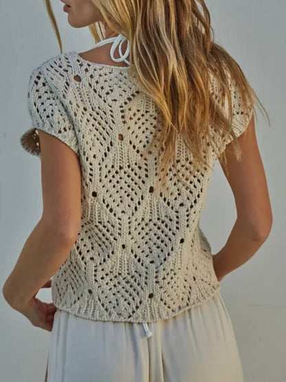 Woman wearing a beige crochet top against a plain background