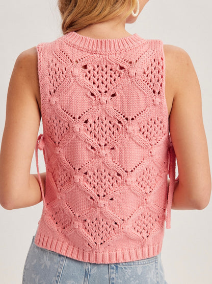 Pink knitted vest with geometric pattern worn by a person on a plain background