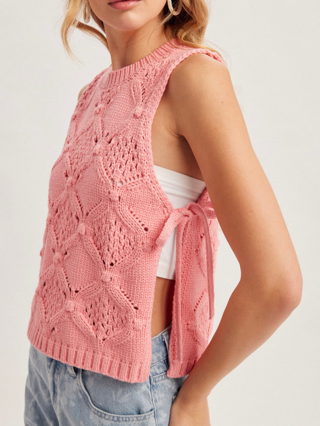 Woman wearing a pink sleeveless knitted top with a white shirt underneath on a light background