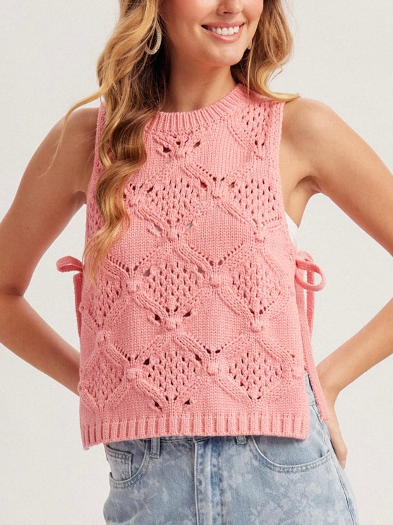 Woman wearing a pink sleeveless knitted top against a plain background