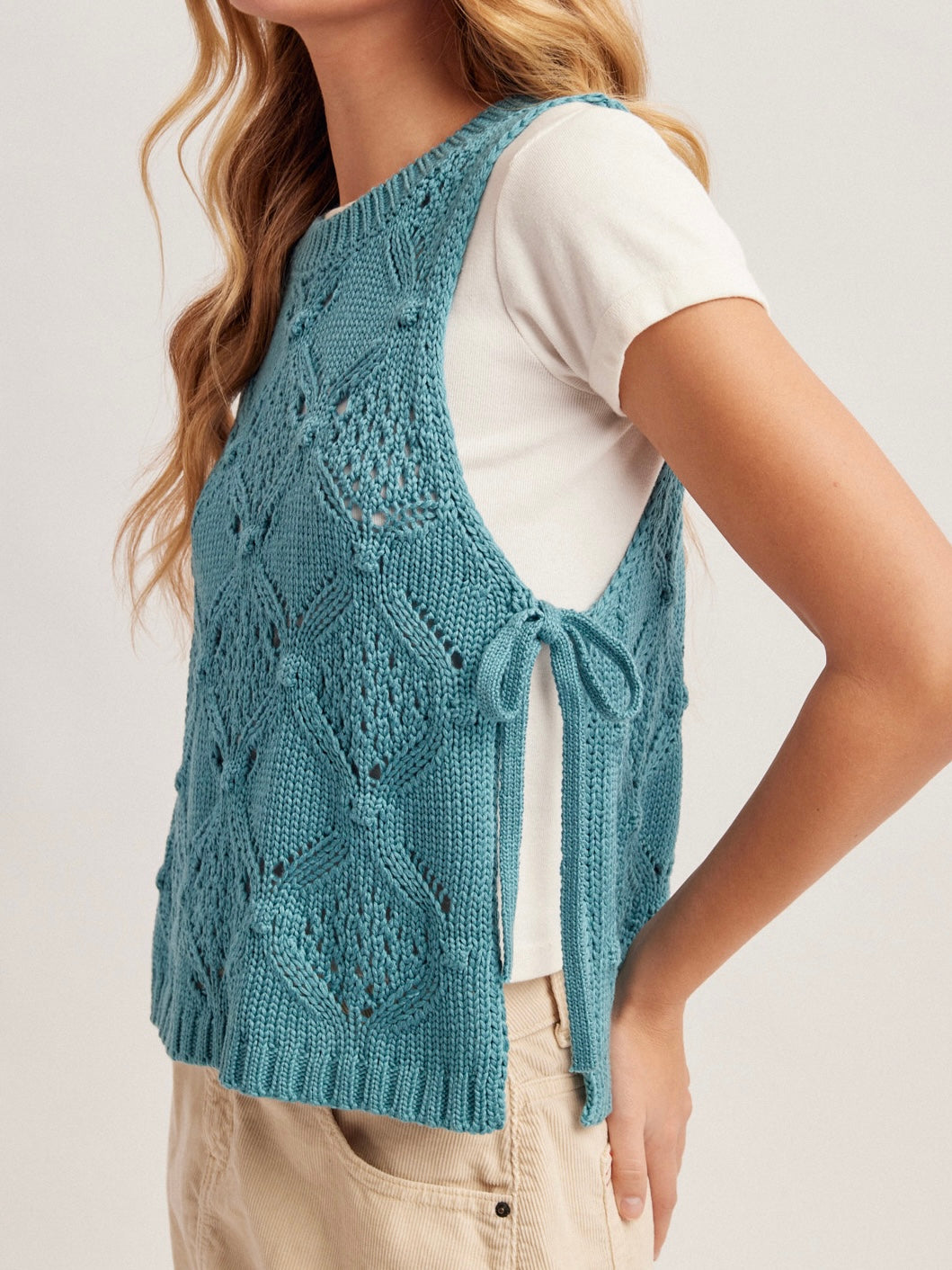 Woman wearing a blue knitted vest over a white shirt on a light background