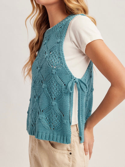 Woman wearing a blue knitted vest over a white shirt on a light background