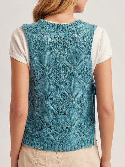 Teal knitted vest with a geometric pattern worn by a person on a light gray background