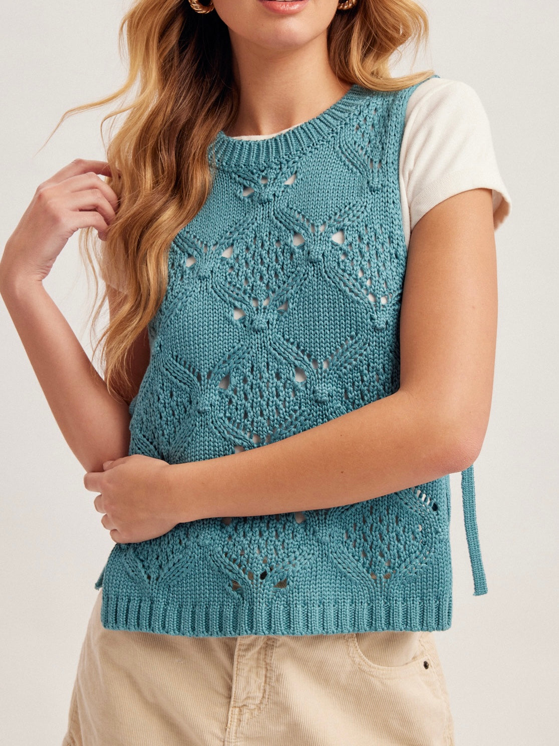 Woman wearing a blue knitted vest with a white shirt underneath on a light background