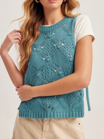 Woman wearing a blue knitted vest with a white shirt underneath on a light background
