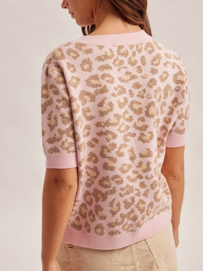 Person wearing a pink sweater with a leopard print pattern on a plain background