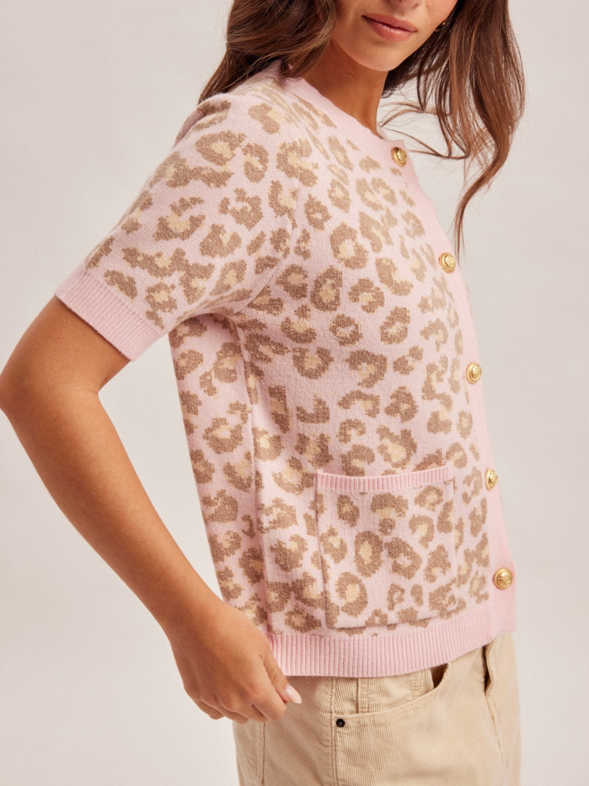 Person wearing a leopard print cardigan with pink trim on a plain background