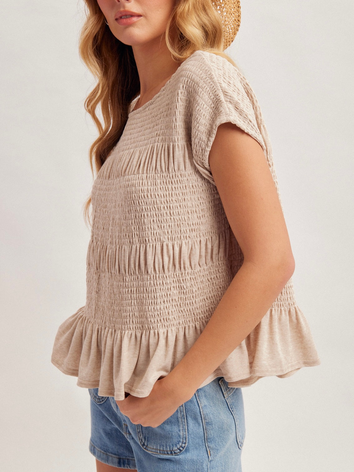 Woman wearing a beige smocked top and denim shorts on a plain background