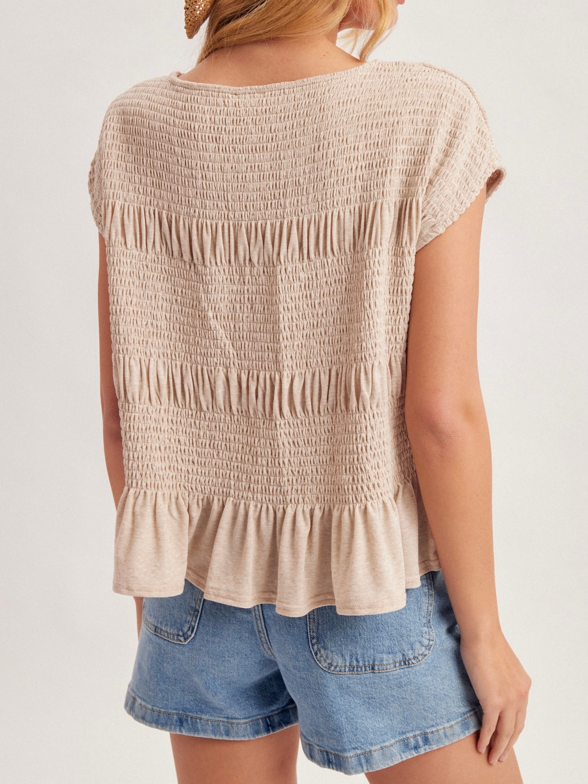 Woman wearing a beige smocked top and denim shorts on a plain background
