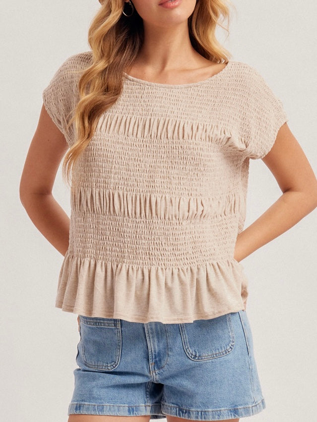 Woman wearing a beige smocked top and denim shorts on a plain background