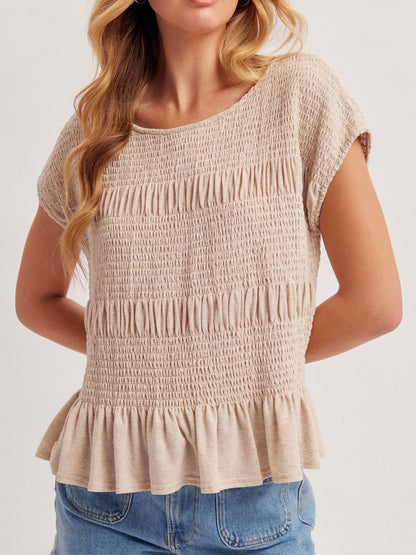 Woman wearing a beige smocked top with blue jeans on a white background