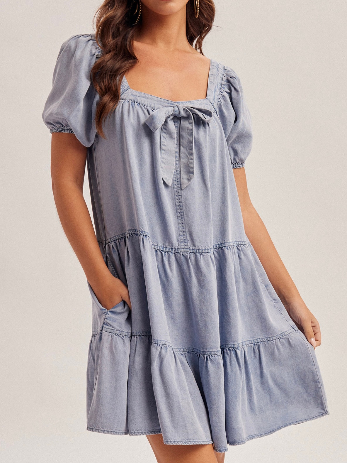 Woman wearing a light blue tiered dress with puff sleeves on a plain background