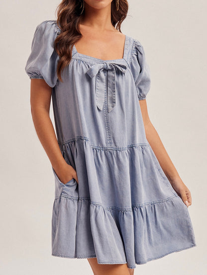 Woman wearing a light blue tiered dress with puff sleeves on a plain background