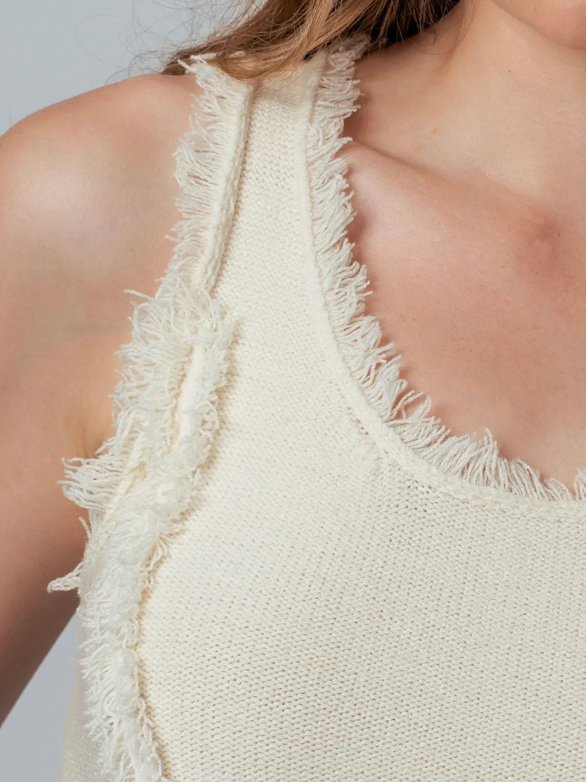 Close-up of a beige sleeveless top with frayed edges on a neutral background
