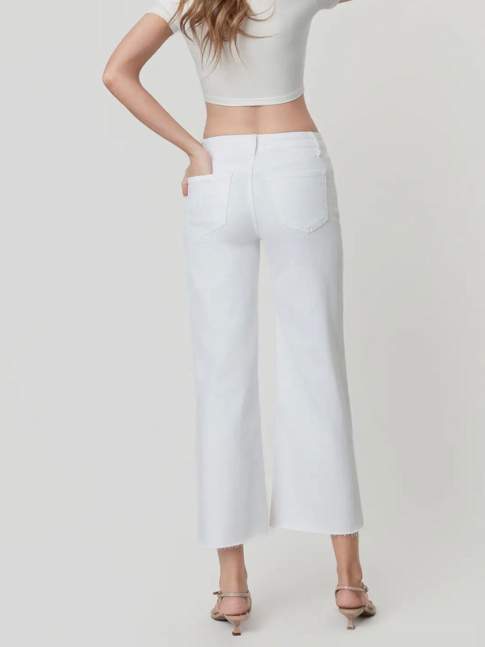 Person wearing a white crop top and white pants on a plain background
