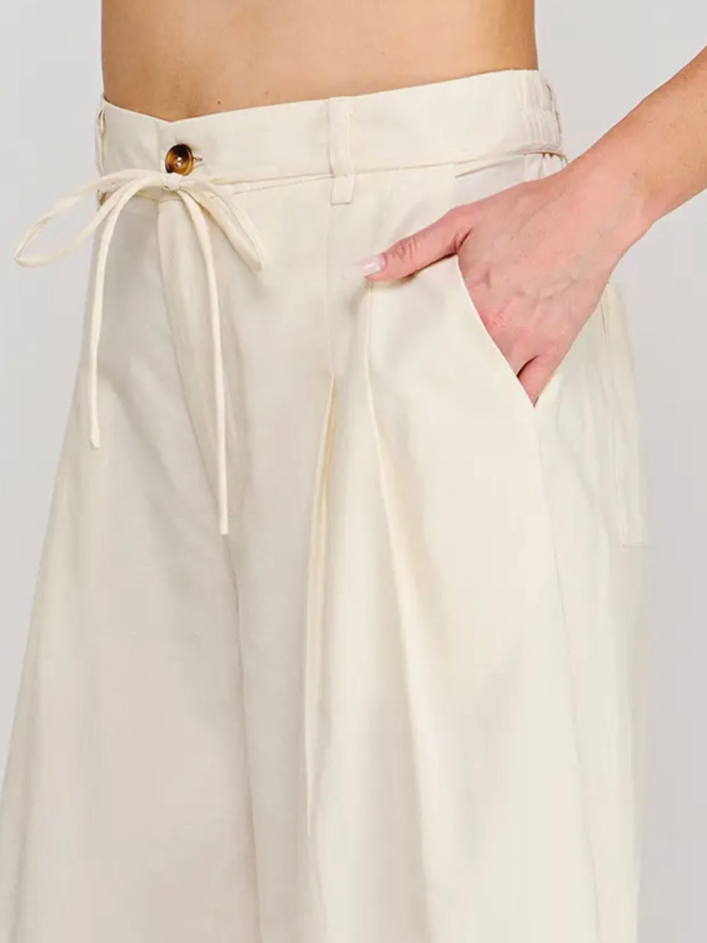 White pants with a drawstring waist and button detail on a plain background