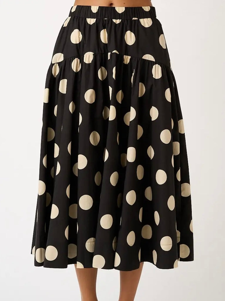 A black midi skirt with a large beige polka dot pattern, shown on a model against a plain white background.
