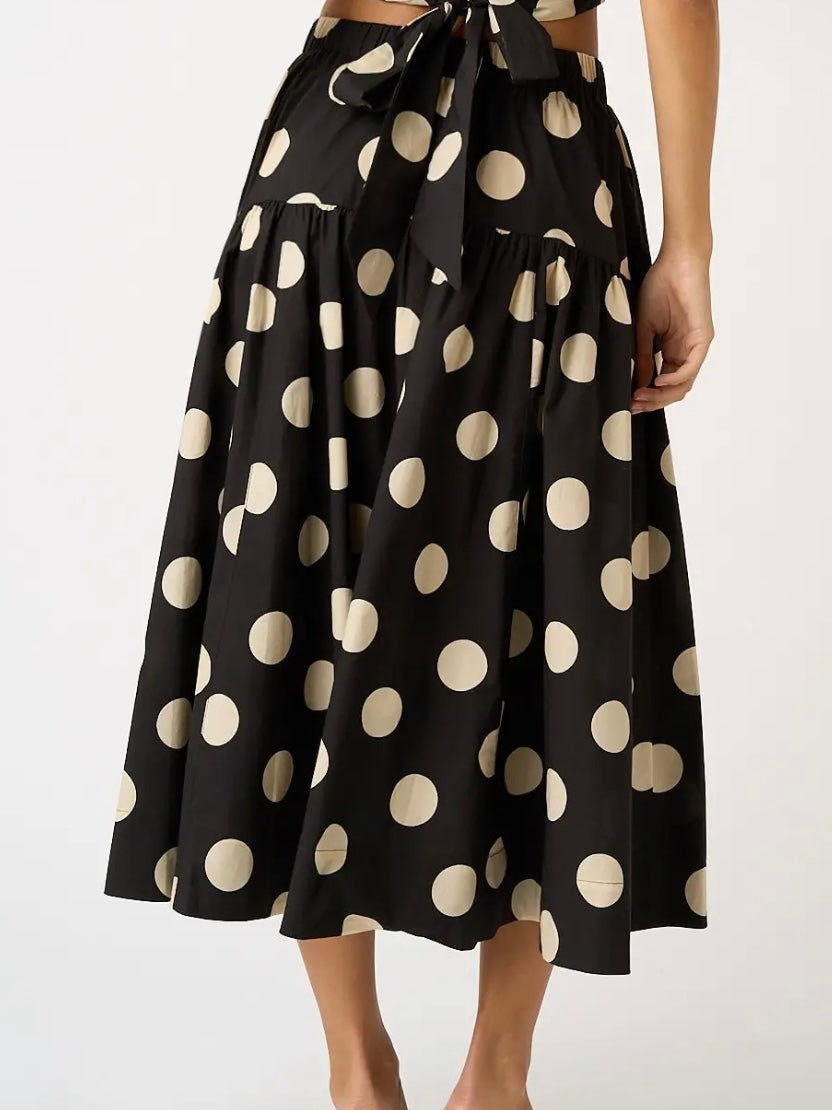 A black midi skirt with large beige polka dots and a tie waist, shown on a model against a plain light background.