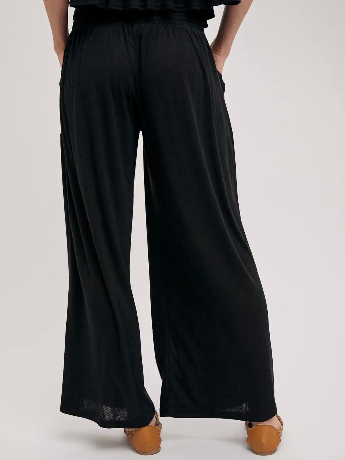Black wide-leg pants with an elastic waistband, shown on a model from the back against a light gray studio background.