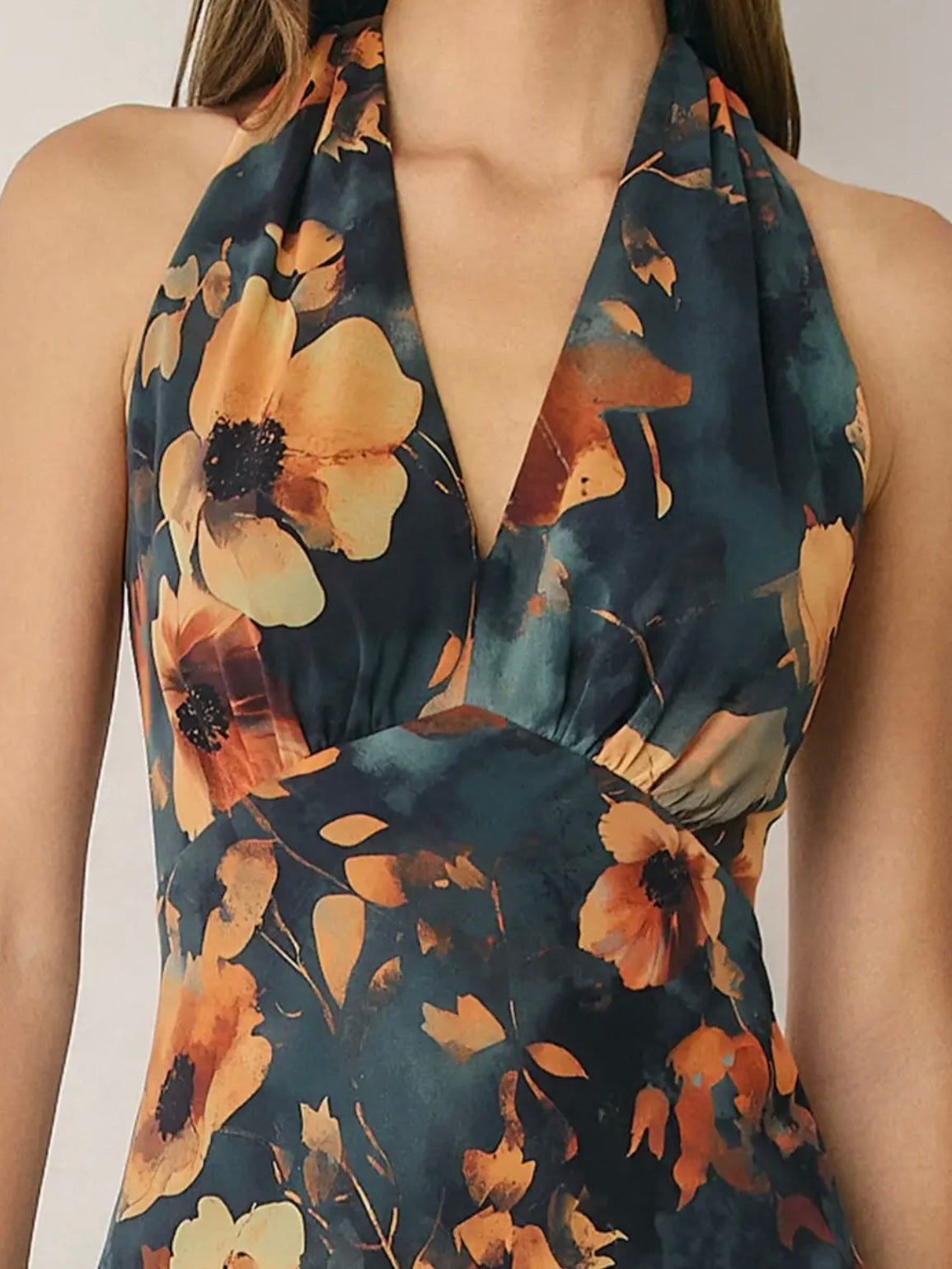 Close-up of a woman wearing a halter-neck dress with a dark teal blue base and a large orange and yellow floral print.