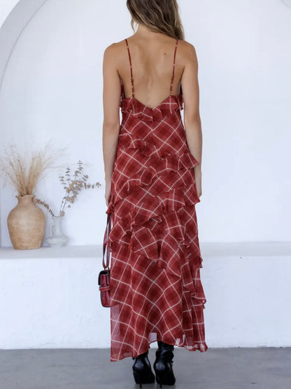 A woman shown from behind wearing a red ruffled maxi dress with a white plaid pattern and thin straps, standing in a bright white room with a vase on a shelf in the background.