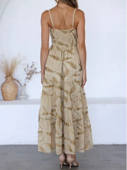 A woman shown from the back wearing a sleeveless, tiered maxi dress with a beige and brown leaf pattern, standing in a minimalist white room.