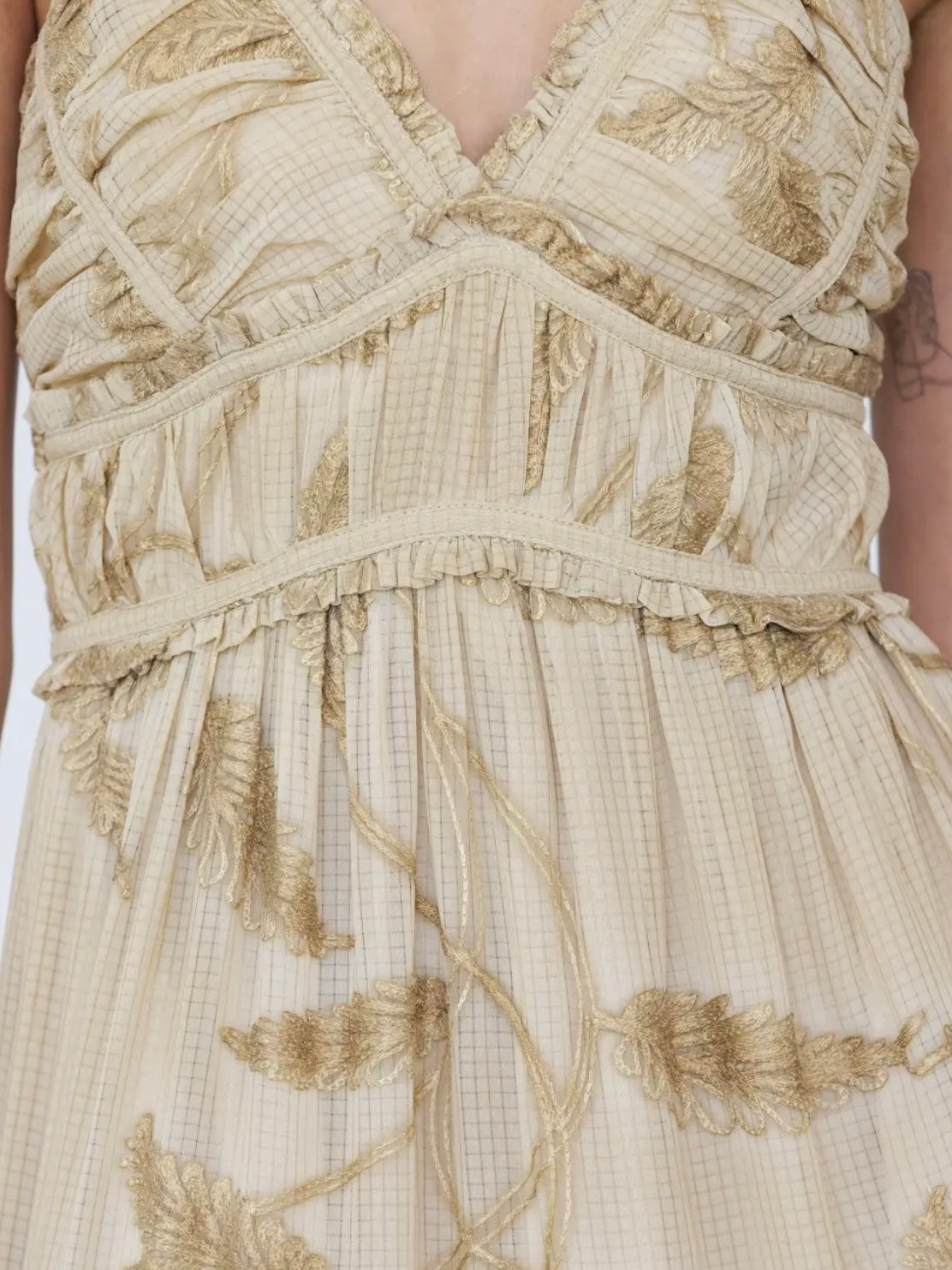Close-up of a beige and gold embroidered dress with ruffles and a textured grid pattern.