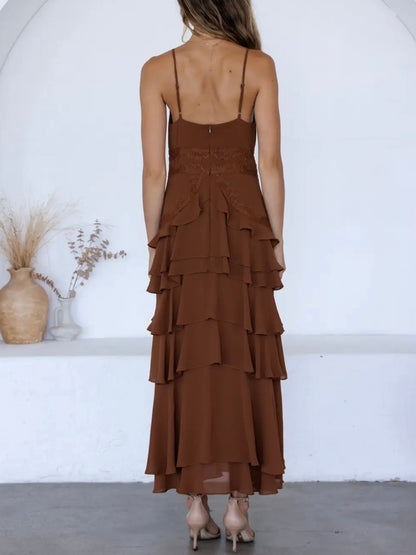 A woman viewed from behind wearing a brown spaghetti-strap maxi dress with a lace-up back and a tiered ruffle skirt, standing in a bright white room.