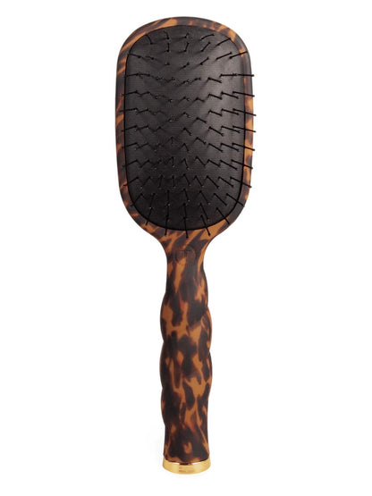 A paddle hairbrush with a glossy tortoiseshell pattern handle and head, featuring a black bristle pad and a gold-toned metal accent at the base, shown against a plain white background.